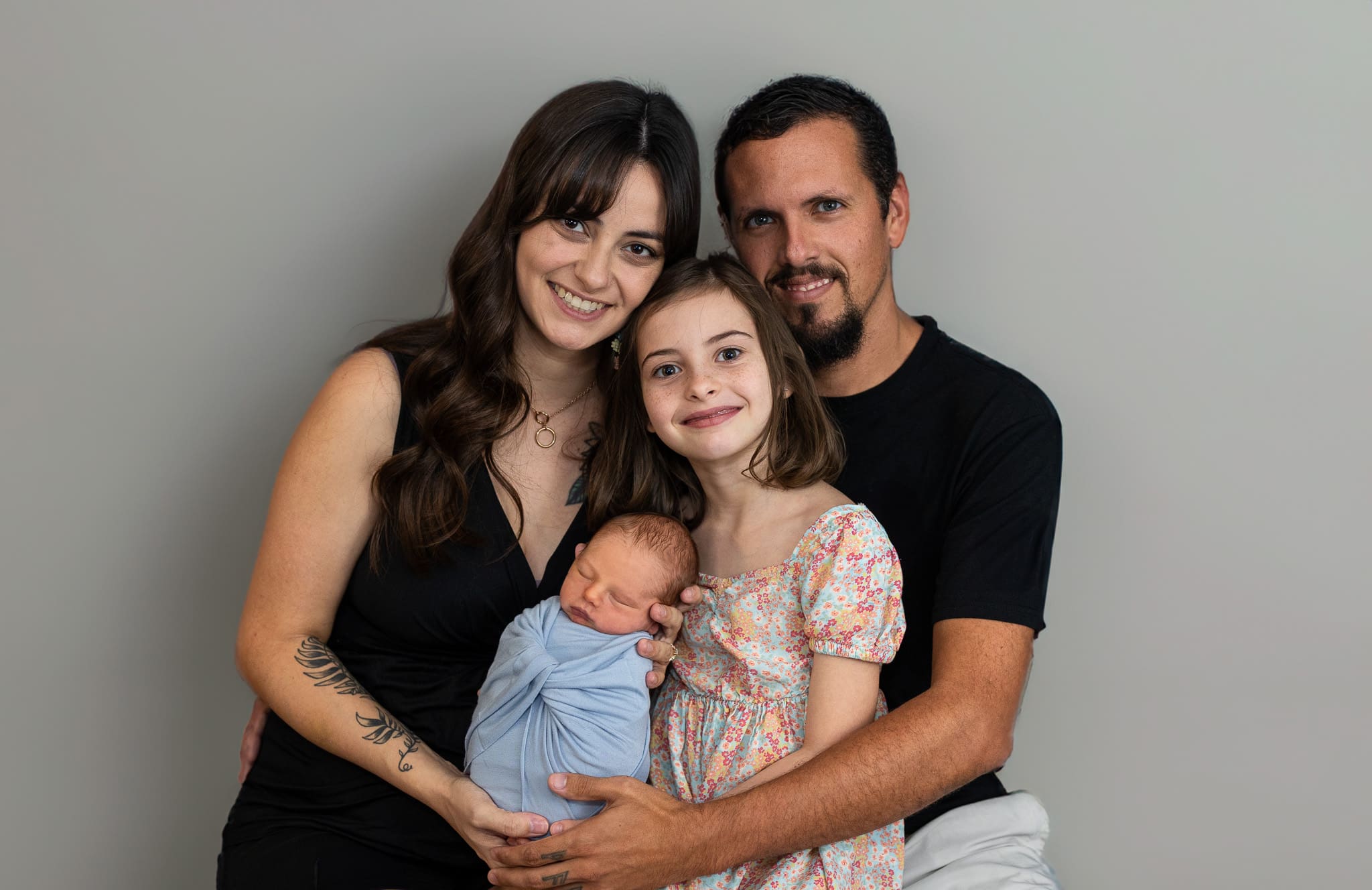 Family of four smiles while holding newborn swaddled in blue during a studio session.