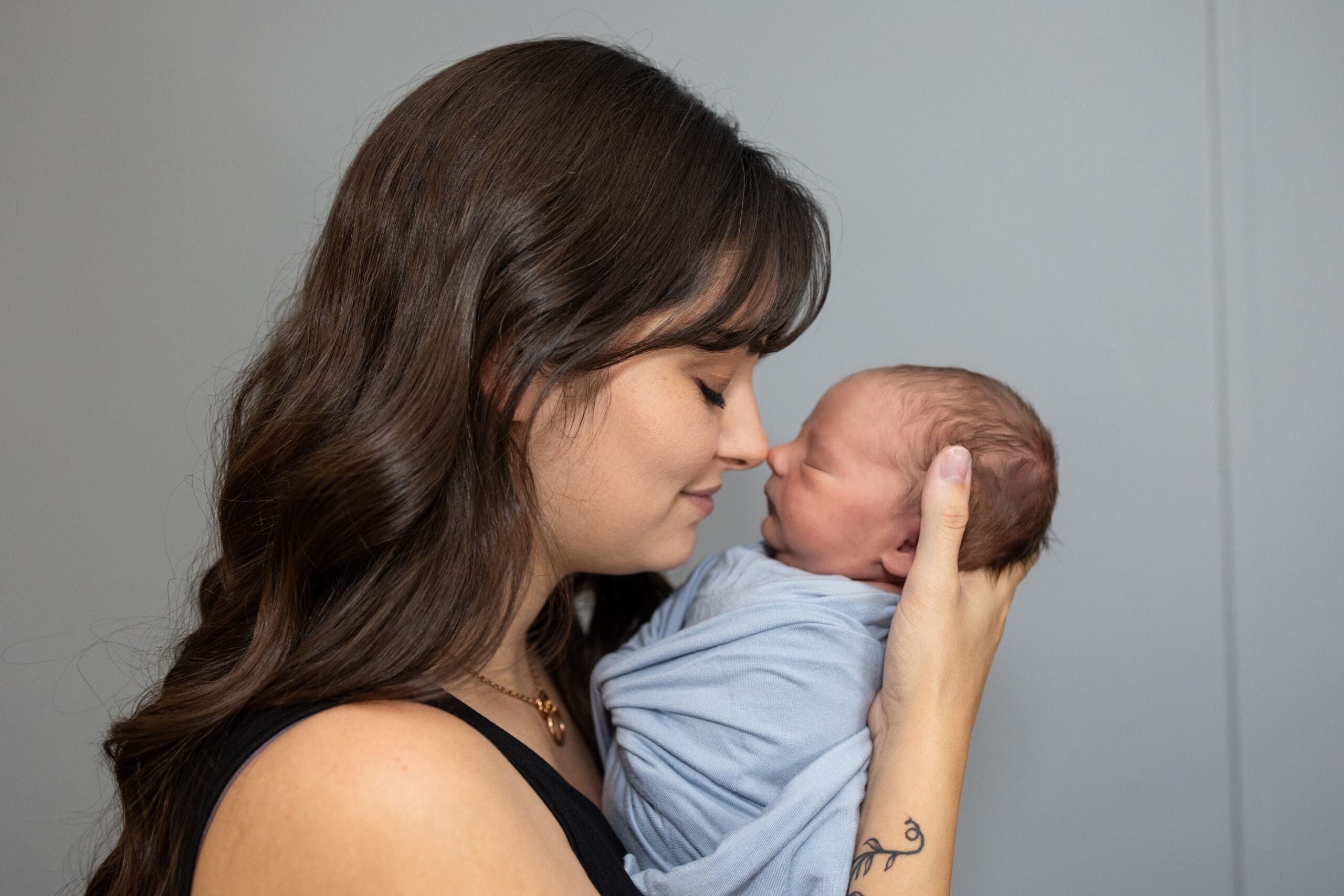 Mother gently holding her swaddled newborn close, touching noses in a tender postpartum bonding moment.